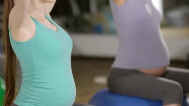 Yan görüş, dengeli bir topun üzerinde oturan, yoga pozisyonu alan ve nefes alma egzersizleri yapan rahat hamile bir kadının görüntüsü.