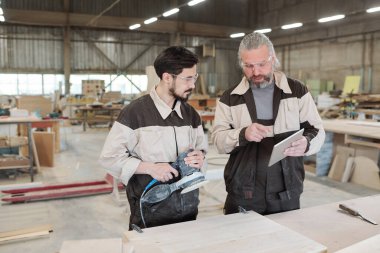 Modern fabrikanın kıdemli işçisi, genç meslektaşına öğütücüyle ahşap işçiliğin nasıl işlendiğini anlatırken dokunmatik ped kullanıyor.
