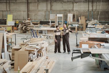 Kıdemli usta ya da ustabaşı yeni endüstriyel işlem makinesini işaret ediyor ve stajyeriyle toplantıda çalışma prensiplerini tartışıyor.