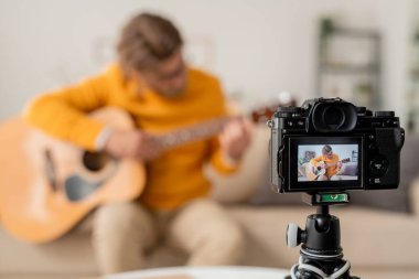 Çağdaş genç müzisyenin kanepede gitar çaldığı video kamera çevrimiçi izleyicilere verdiği dersi çekiyor.