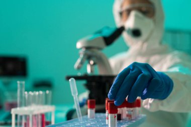 Koruyucu kıyafetli laboratuvar çalışanının yakın çekimi Coronavirus hastalarının kanını incelerken test tüpünü rafa koyuyor.
