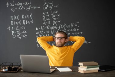 Genç öğretmen ya da öğrenci ellerini başının arkasında tutarken online cebir dersi sırasında dizüstü bilgisayara bakıyor.