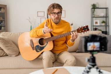 Genç sakallı müzik öğretmeni ev ortamında bir şey anlatıyor ya da çevrimiçi izleyici sorununa cevap veriyor.