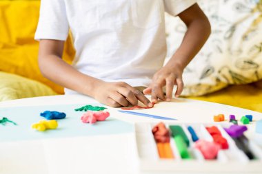 Afrikalı ya da melez ilkokul öğrencisinin elleri ya da kağıt üzerinde resim yaparken masaya plasticin döken anaokulu öğrencisinin elleri.