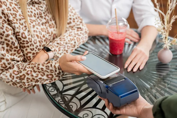 年轻优雅的女性手拿着智能手机 拿着小玩意放在付款终端上 一边在咖啡店里支付酒钱 — 图库照片