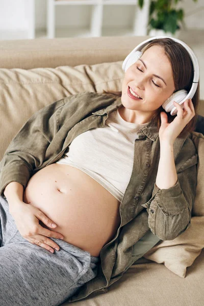 Joven Mujer Embarazada Serena Con Auriculares Tumbados Sofá Escuchando Música —  Fotos de Stock