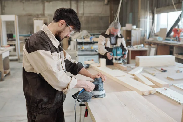 年轻的工厂工人使用磨床使工件表面光滑 并准备好木板供进一步加工 — 图库照片