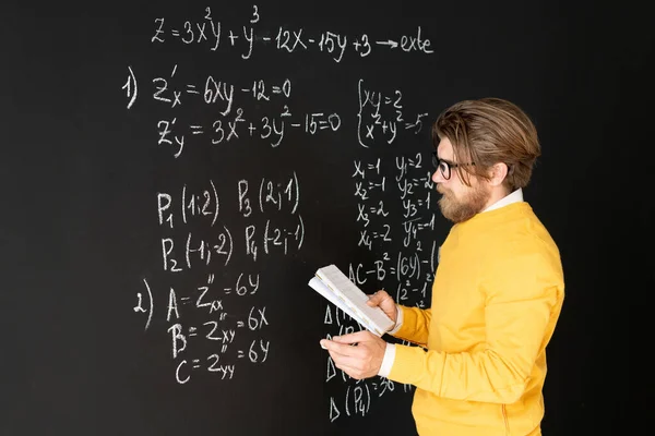 留胡子的老师在把任务交给他的网上听众之前 在黑板上随意重写公式 — 图库照片