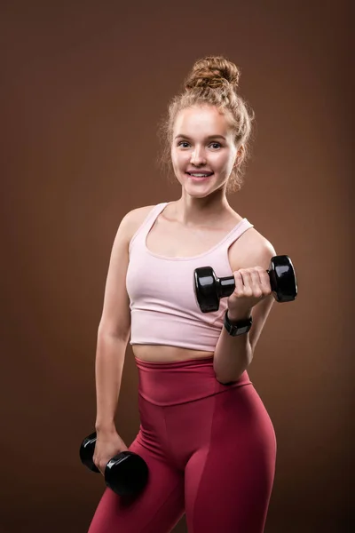 ジムやスポーツクラブでのトレーニング中に孤独の中で運動中にダンベルを持ち上げるアクティブウェアの若い陽気なスポーツ女性 — ストック写真