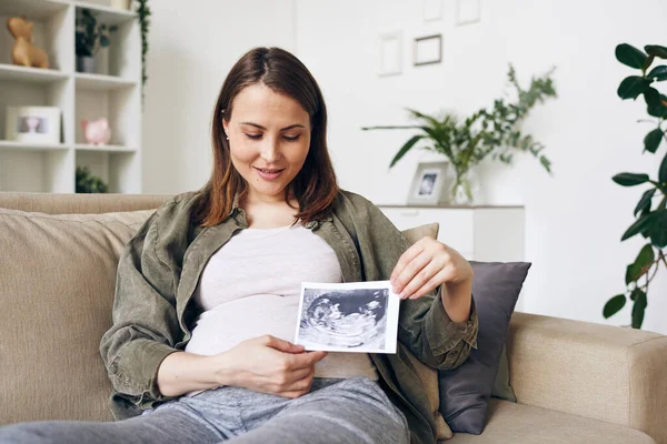 Współczesna Kobieta Ciąży Pokazuje Ultradźwiękowy Obraz Przyszłego Dziecka Patrząc Niego — Zdjęcie stockowe