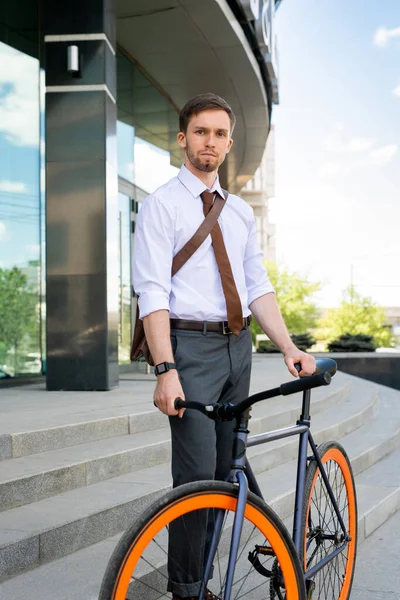 シリアス男でシャツ ネクタイとズボン立っています彼の自転車でカメラの前にオフィスを離れ 仕事の日後に家に帰る — ストック写真