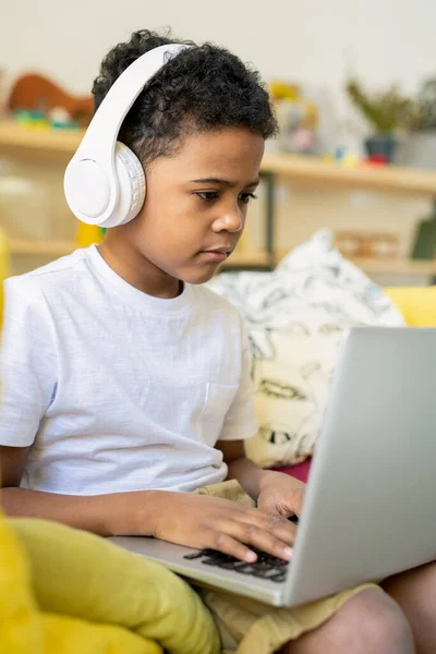 Ernstige Basisschooljongen Van Afrikaanse Afkomst Met Koptelefoon Typen Laptop Tijdens — Stockfoto