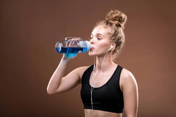 トレーニングやジョギングの後 カメラの前でペットボトルから飲むトラックスーツの若い喉の渇きのスポーツ女性にフィット — ストック写真