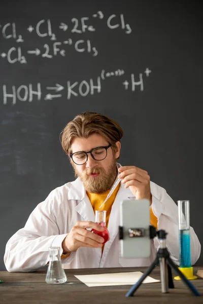 年轻的专业化学家坐在智能手机摄像机前 用粉红液体物质把液体倒入嘴中 — 图库照片