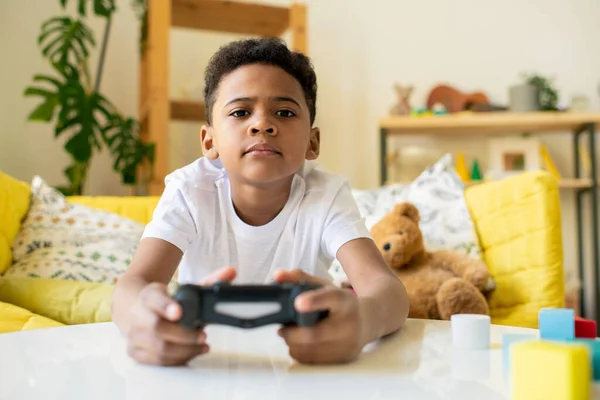 Sério Bonito Mestiço Menino Com Joystick Sentado Mesa Sala Estar — Fotografia de Stock