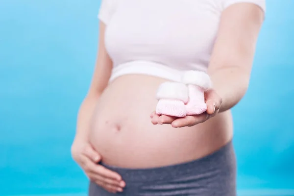 年轻孕妇的手 给你看一双温暖的小针织袜子 给将来的宝宝穿 同时单独摸她的肚子 — 图库照片