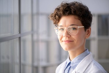 Modern laboratuarda ayakta duran, gözlüklü, gülümseyen, zeki kadın sağlık görevlisinin portresi.