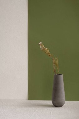 Gri seramik ya da kuru kır çiçekleriyle el yapımı vazo. Metnin için telif alanı olan çift renkli duvara karşı beyaz masada duruyor.
