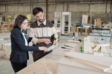 Üniformalı ve koruyucu gözlüklü genç işçiler yeni mobilya taslağını gösterip meslektaşlarına dışlıyorlar.