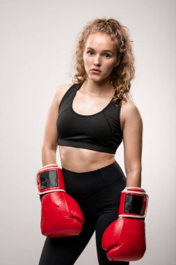 Siyah eşofmanlı ve kırmızı boks eldivenli sarışın kız yalnız başına kameranın önünde spor kulübünde veya spor salonunda eğitime hazır bekliyor.