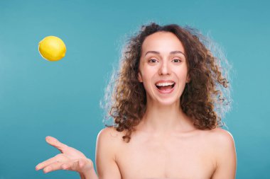 Çıplak omuzlu, siyah kıvırcık saçlı, taze limon fırlatan ve mutluluğu ifade eden genç ve neşeli bir kadın.