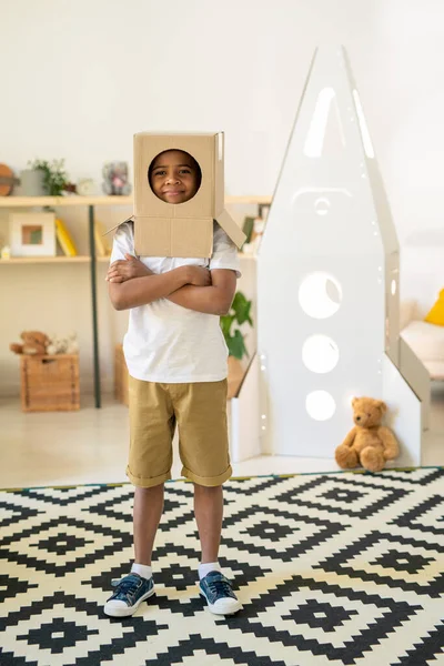 一个快乐的小男孩 头上顶着纸盒 站在客厅的地毯上 从圆孔里望着你 — 图库照片