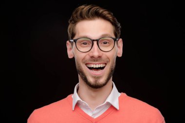 Kirli sakallı, siyah arka planda duran gözlük takan kendinden geçmiş bir gencin portresi.