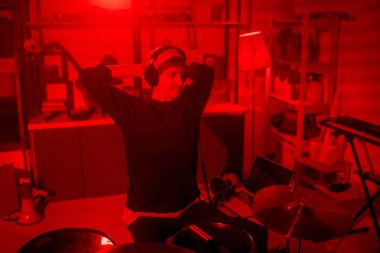 Rahat giyimli ve kulaklıklı genç müzisyen stüdyosunda bateri başında otururken kaydettiği müziği dinliyor.