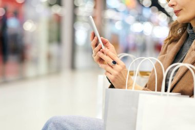 Alışveriş merkezinden alışveriş yaptıktan sonra akıllı telefondaki reklamlara bakan gündelik giysiler içindeki zarif bayan müşterilerin elleri.