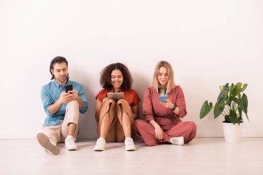 Genç çağdaş çağdaş çağdaşlardan oluşan bir grup boş vakitlerinde duvarın önünde oturmuş akıllı telefonlar ve touchpad 'lerde kayıyorlar.