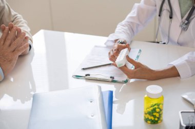 Whitecoat 'taki genç klinisyenlerin elleri, ne sıklıkta kullanması gerektiği konusunda hastalara danışmanlık yaparken masasında hap taşıyan plastik kapları tutuyorlar.