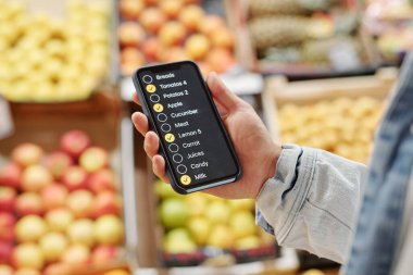 Çiftçi pazarından yiyecek alırken kontrol listesi uygulaması kullanan tanınmayan bir adamın yakın plan fotoğrafı.