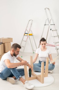 Genç çift yeni eve taşınıyor yerde oturuyor ve birlikte kahve masası kuruyorlar.