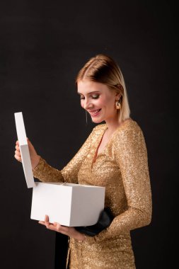 Zarif elbiseli mutlu genç bayan hediye kutusunu çıkarıyor ve arkadaşlarının ya da erkek arkadaşının doğum günü hediyelerine bakıyor.