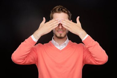 Turuncu kazaklı genç adam saklambaç oynarken ya da korkarken elleriyle gözlerini kapatıyor.