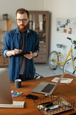 Masada sakallı ve dijitalistle çalışırken bilgisayar monitörüne bakan odaklanmış genç grafik tasarımcısı