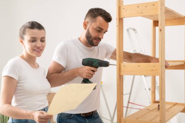 Hoşnut genç bir kadın yeni bir dairede mobilya montajında kocasına yardım ederken okuma dersleri alıyor.