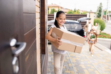 At kuyruklu mutlu bir kızın portresi büyük bir kutu tutuyor ve yeni evin kapısında duruyor.