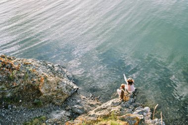 Genç bayan sırt çantalı gezileri sırasında sırt çantasıyla kocasına yakın çömelme yerlerinde otururken uzak nehir kıyısını işaret eden bir gezgin.