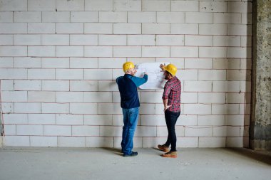 İki profesyonel mühendis tuğla duvarın yanında duruyor ve iş toplantısında tamamlanmamış binanın eskizini tartışıyorlar.