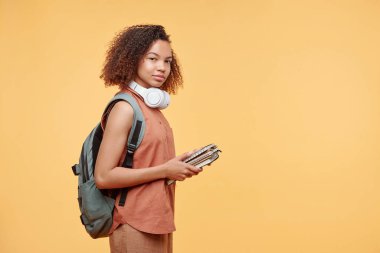 İçerik portresi Afro saçlı siyah liseli kız çalışma kitaplarını sarı arka planda tutuyor