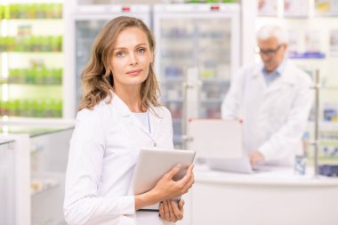 Genç profesyonel eczacı ve büyük eczane asistanı iş sırasında gerekli ilaçları aramak için touchpad kullanıyor.