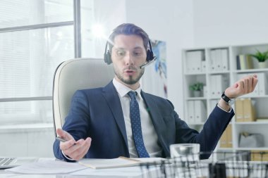 Genç servis destek operatörü modern ofiste elsiz cihaz kullanarak müşteriyle konuşuyor.