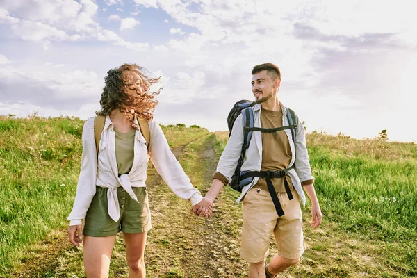 Yaz günü bulutlu gökyüzüne karşı kır yolunda yürürken günlük kıyafetlerle sohbet eden ve birbirlerine bakan genç aşıklar.