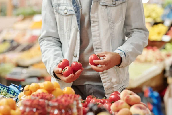 フードカウンターに立って有機市場で新鮮なトマトを取るジャケットの認識できない男のクローズアップ — ストック写真