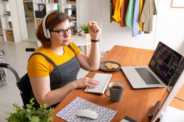 Jonge Vrouwelijke Programmeur Zit Thuis Achter Het Bureau Eet Koekjes — Stockfoto