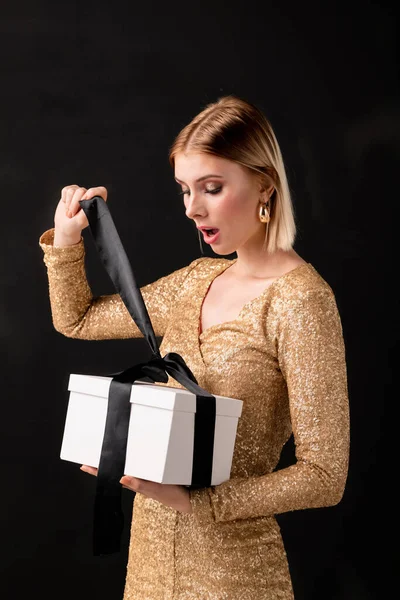 Parlak elbiseli zarif bayan siyah ipek kurdeleyi çözüyor beyaz gftbox bağlıyor ve doğum günü hediyesini dört gözle bekliyor.