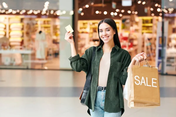 Joven Comprador Alegre Con Bolsas Papel Mostrando Tarjeta Crédito Mirándote —  Fotos de Stock