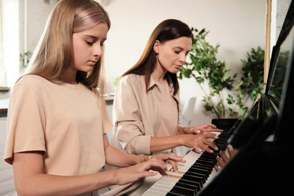 深刻なブロンドティーン少女プッシュキーのピアノ中に訓練中にホームレッスンの音楽とともに彼女のお母さん座って近くに — ストック写真