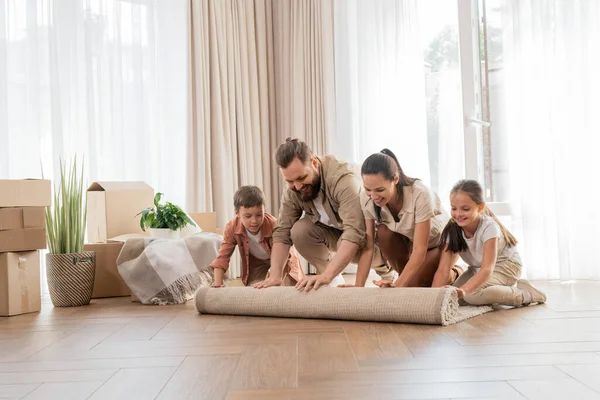 搬进新房子后 一家人带着两个孩子在新客厅里铺上地毯 — 图库照片